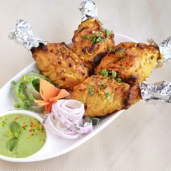 Four Tandoori chicken drumsticks with foil-wrapped bones, served with mint chutney and sliced onions.